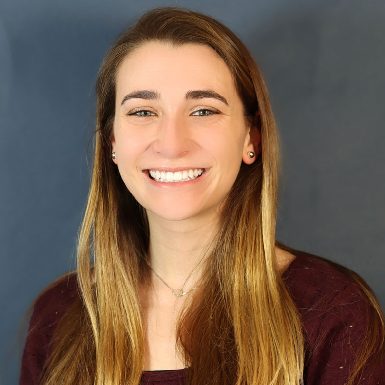 Geena Holdcraft Headshot of woman with long hair in burgandy top and blue background