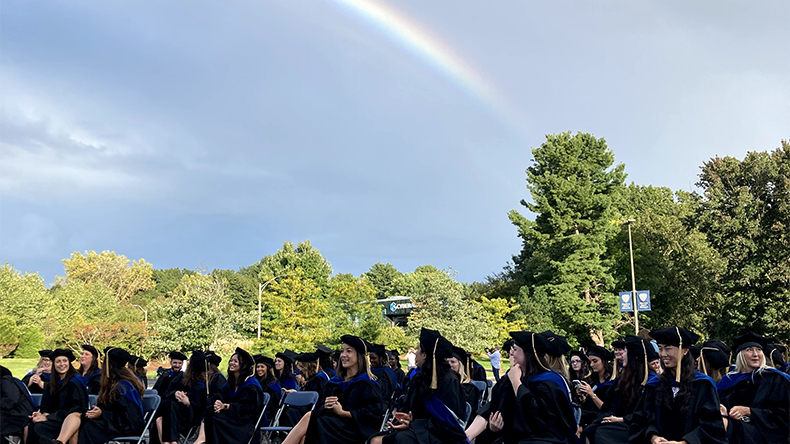 A graduating class outside on a sunny day with a rainbow