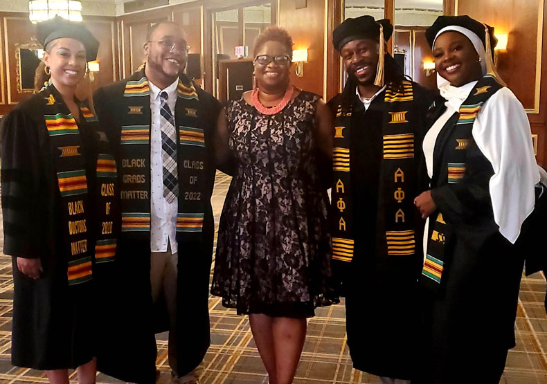 Five standing adults, four in commencement regalia