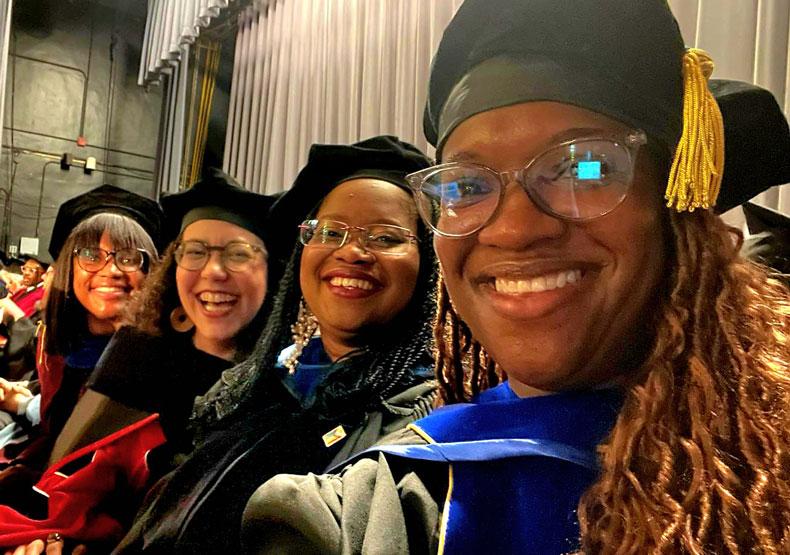 Four women smiling at camera in commencement regalia