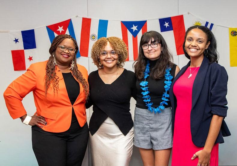 Four women posing for camera with a banner of flags behind them
