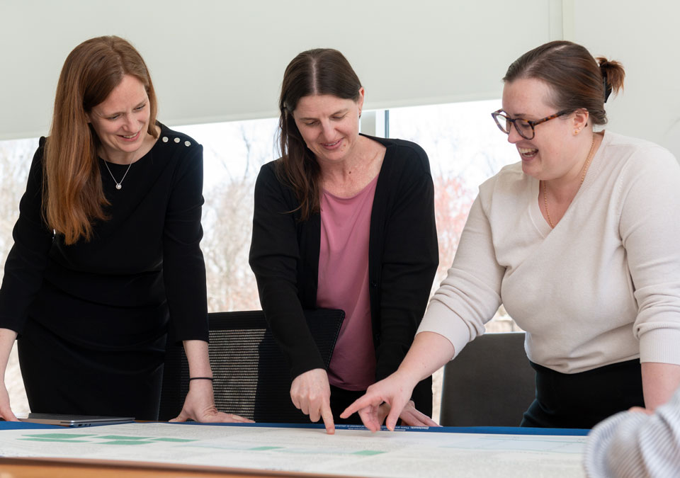 Three women talking and pointing at large diagram on conference table