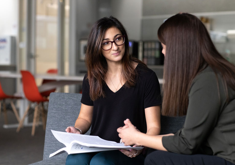 two women sitting in an open area sharing a document