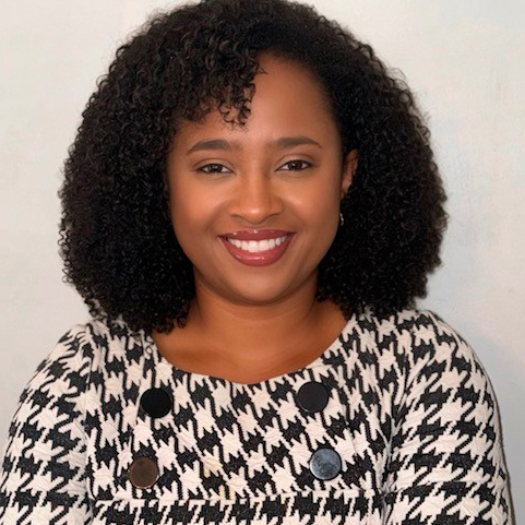 Portrait photo of smiling black woman with shoulder length dark brown curly hair and houndstooth top