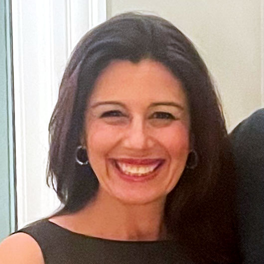Portrait photo of smiling woman with shoulder-length dark brown hair, black top and neutral background
