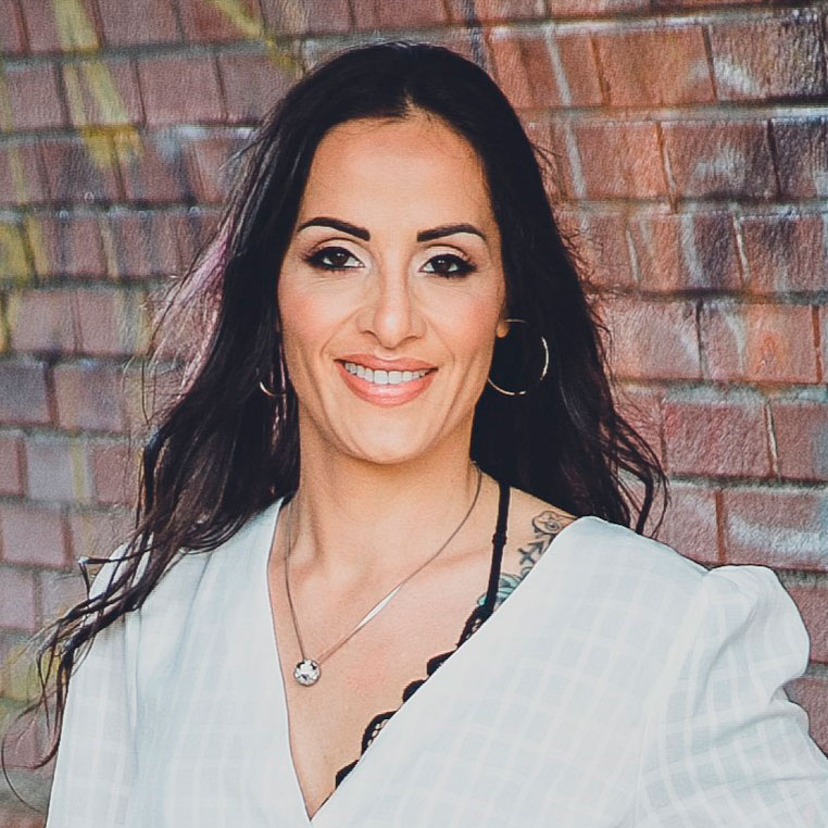 Portrait photo of woman with long dark brown hair smiling with a brick background