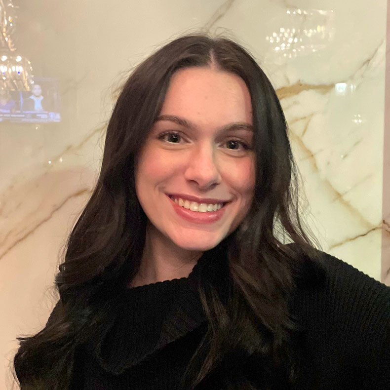 Profile photo of Chloe Stanfa smiling in dark brown sweater and beige background