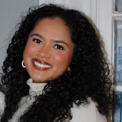 Profile photo of Tanu Kumar with brown curly hair, smiling in white sweater and neutral background