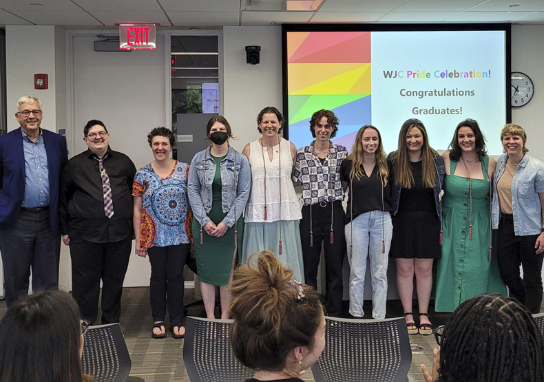 2024 LGBTQIA+ Graduates group of men and woman standing in front of a classroom