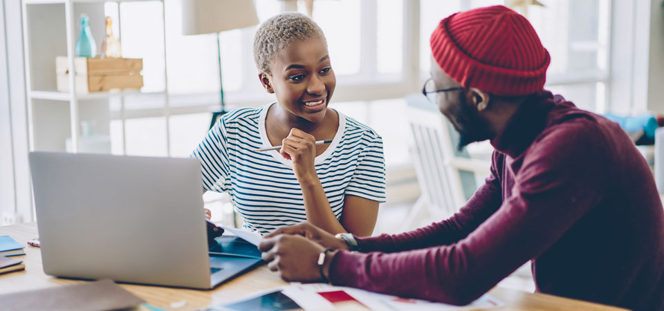 two young people talking at table in front of laptop