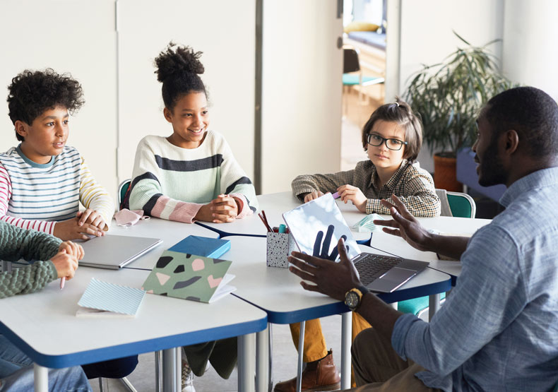 male teacher talking to students at table