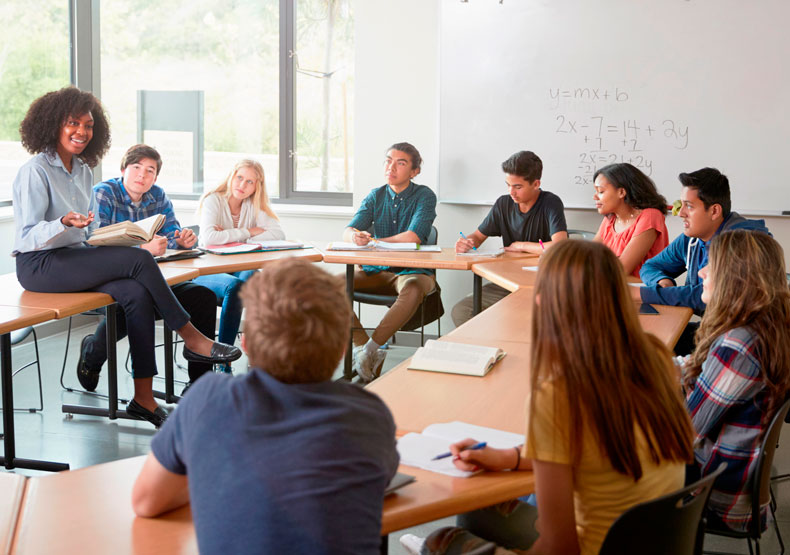 female teacher sitting on table talking to classroom of students