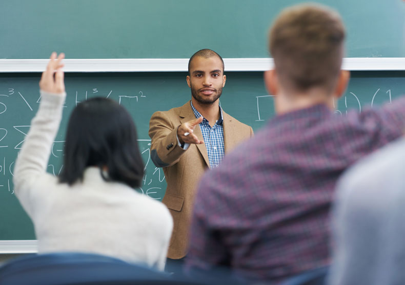 Teacher in front of classroom with chalkboard behind him