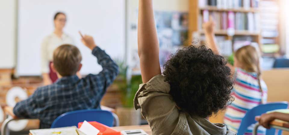 Children in a classroom raising hands