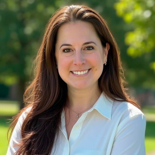 Outdoor portrait photo of woman smiling, with long brown hair, 