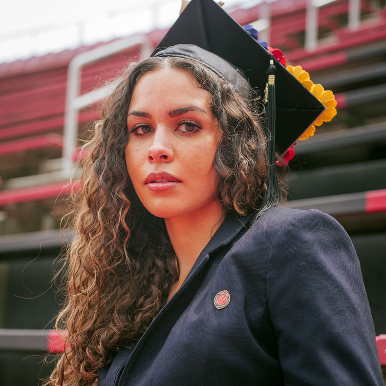 Portrait of woman sitting in stadium bleachers with cap and gown