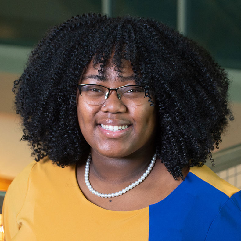 Portrait photo of woman with dark hair, glasses, and a blue and gold top