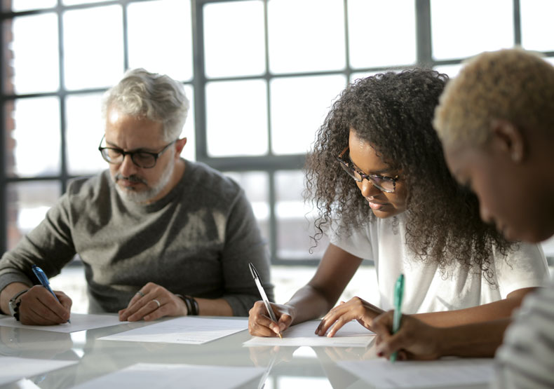 three people working at a table with their heads down