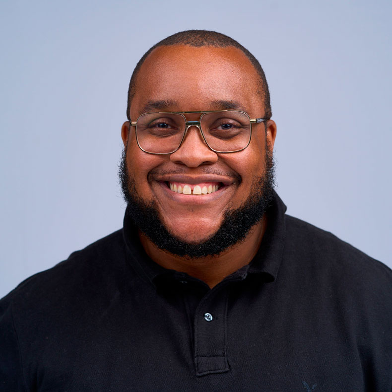 Portrait photo of smiling man with glasses and beard with light blue background