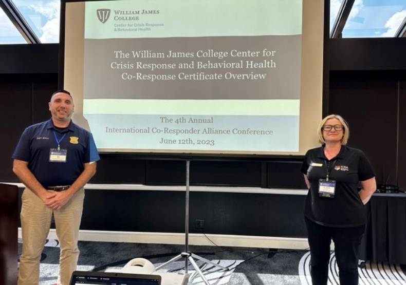 SGT. Jay Ball and Dr. Sarah Abbott. smiling in front of large screen showing their presentation.