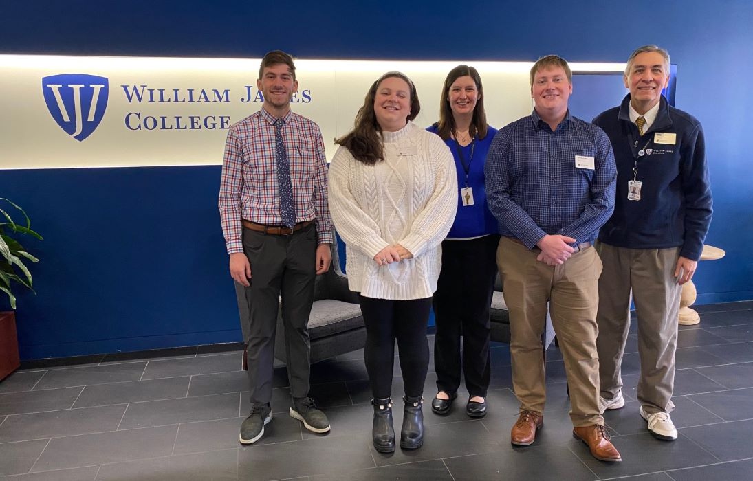 Photo of five people standing in front of a William James College logo