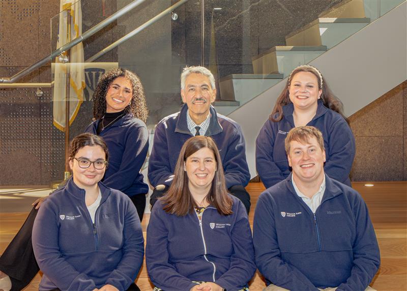 Photo of six admissions staff wearing matching William James College zip up sweaters.