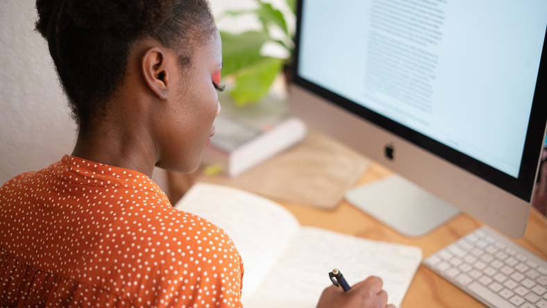 Woman sitting at a computer, writing in a notebook