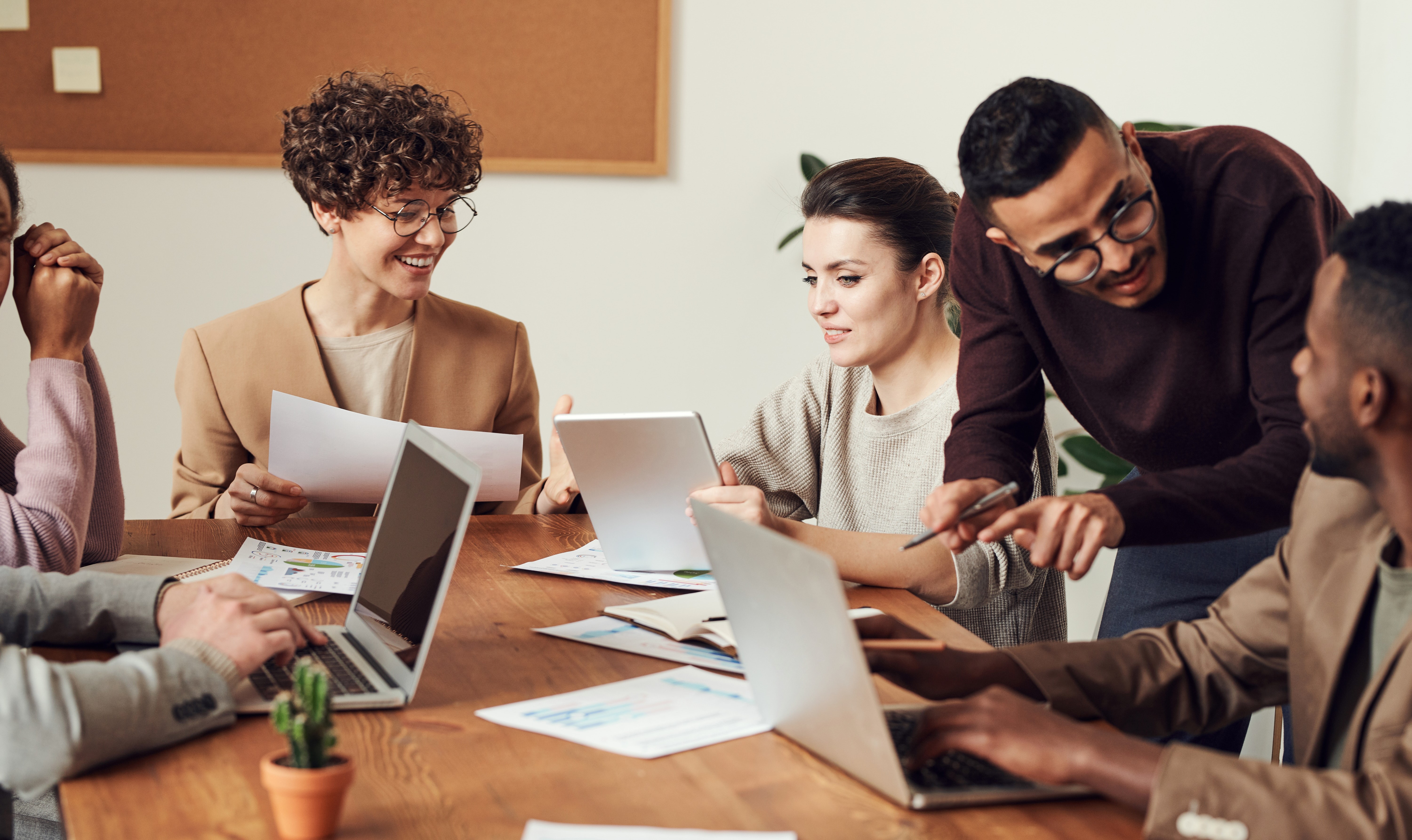 six people working together at at table with papers and laptops