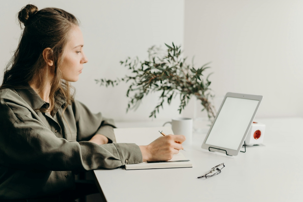 Photo of young woman sitting at a table with a notebook and tablet