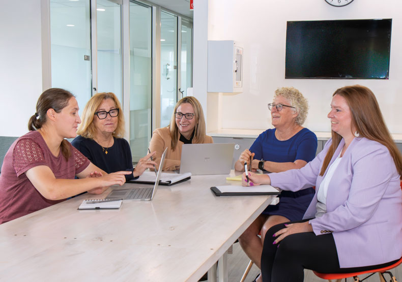 Four women sitting around a table with laptops and notebooks