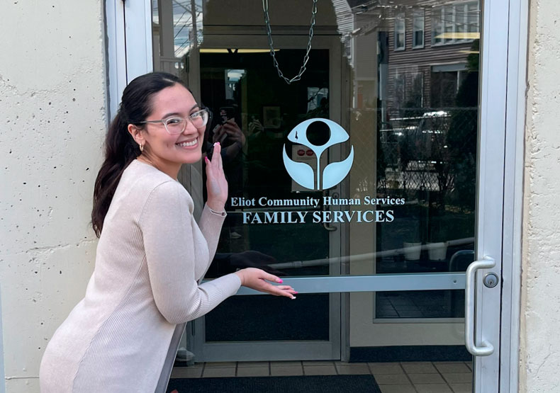 woman holding up hands and smiling in front of agency door