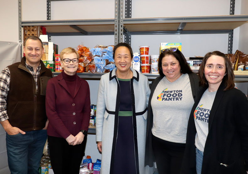 Five people smiling and standing in front of shelves with canned food