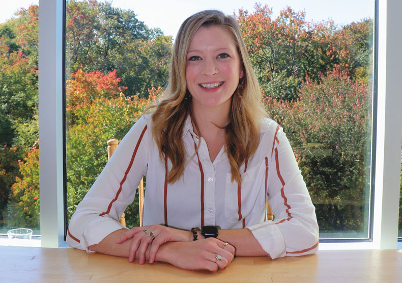 woman sitting at table and smiling with fall colors behind her in window