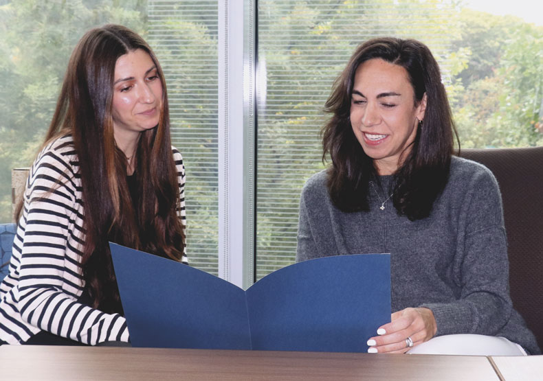 two woman sitting at a table smiling, and holding a document 