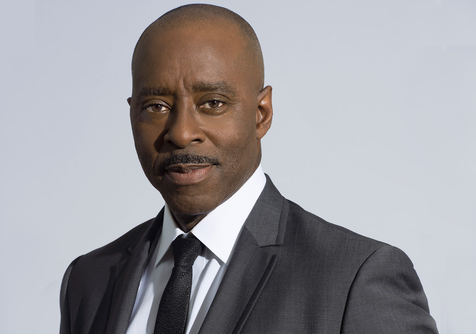 Black man in gray suit and gray background posing for camera