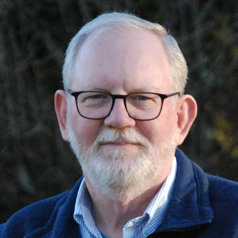 Portrait photo of man smiling, in blue jacket, wearing glasses with a dark background