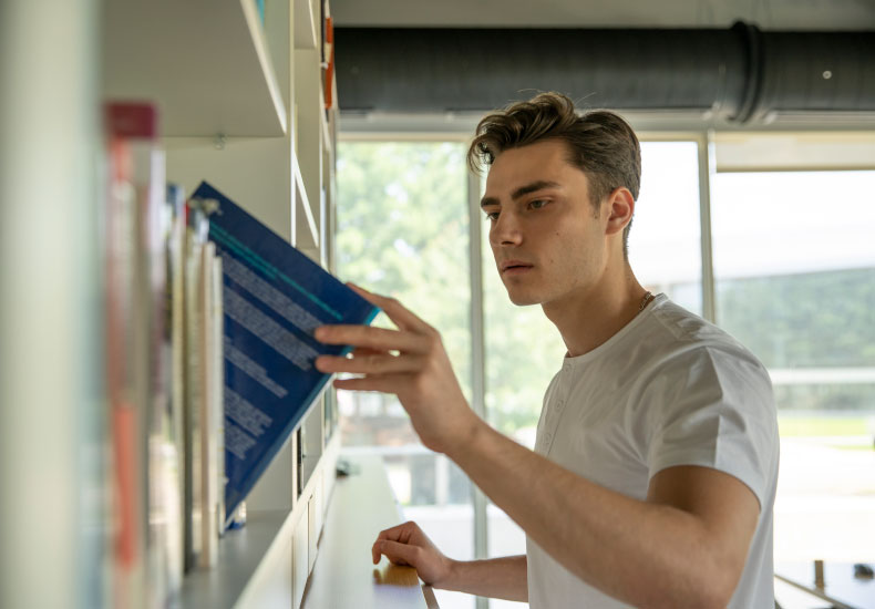 Adult male in white t-shirt pulling a book out of a library stack